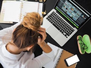 A woman holds her head in frustration while staring at her computer.