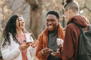 Three friends laugh while having a conversation in the park.
