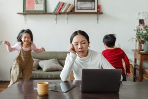 A woman tries to concentrate on her work while her children run around in the background.
