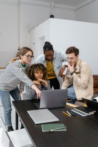 A team of people sit around a computer, working together on a problem.