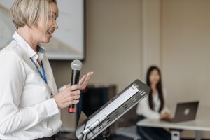 A woman stands at a lectern, giving a presentation.