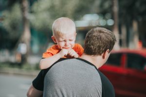A boy crying, as he is being carried by his father.