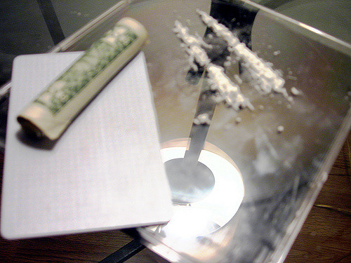 Two lines of cocaine on a mirror with a dollar bill rolled up next to it.