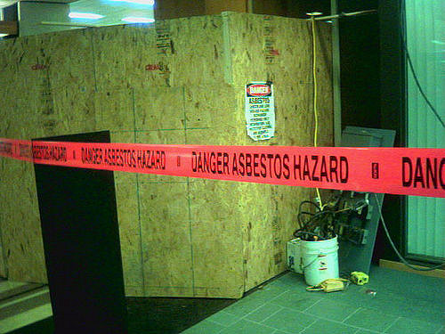 A construction zone with a red tape across it reading: Danger Asbestos Hazard