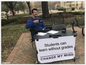 Photo of a man sitting at a folding table. Title: Students can learn without grades; Change my mind.