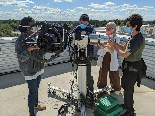 Three students hold a telescope in place while a fourth rebalances it.